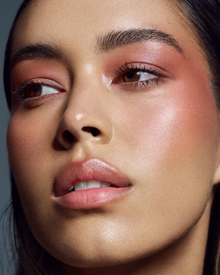 Closeup of a young woman with dewy skin, wearing pink blush on her cheeks and eyelids.